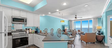 A modern kitchen with white cabinets, a central island, and a dining area with a view.