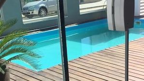 Blick auf ein Schwimmbecken mit Holzterrasse, einem Blumentopf und einem Auto im Hintergrund.