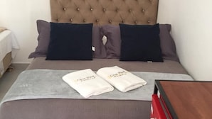 Ein ordentlich bezogenes Bett mit einer gebügelten Kopfteil, zwei Kissen, einer grauen Decke und zwei Handtüchern mit dem Schriftzug 'Casa Park'.