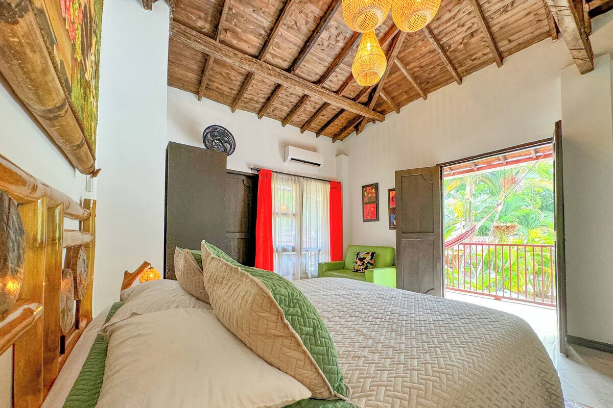 Un dormitorio con una cama grande, un sofá verde, techo de madera y vistas a espacios verdes.