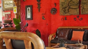 Ein Zimmer mit einer roten Wand, die mit verschiedenen Gegenständen dekoriert ist, ein Holzstuhl, ein Ledersofa und ein kleiner Tisch mit einer Pflanze.