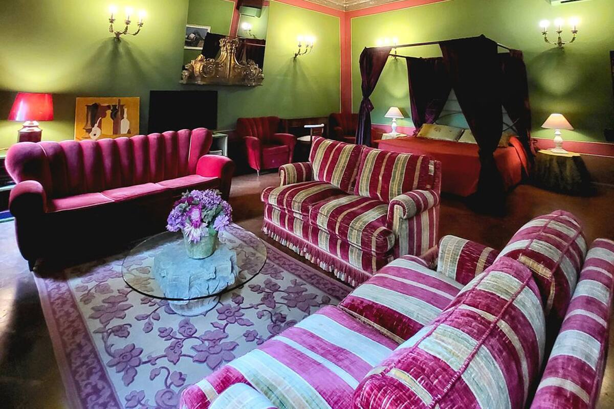 A room with green walls, a red and white striped sofa, a pink sofa, a bed with a canopy, and a chandelier.