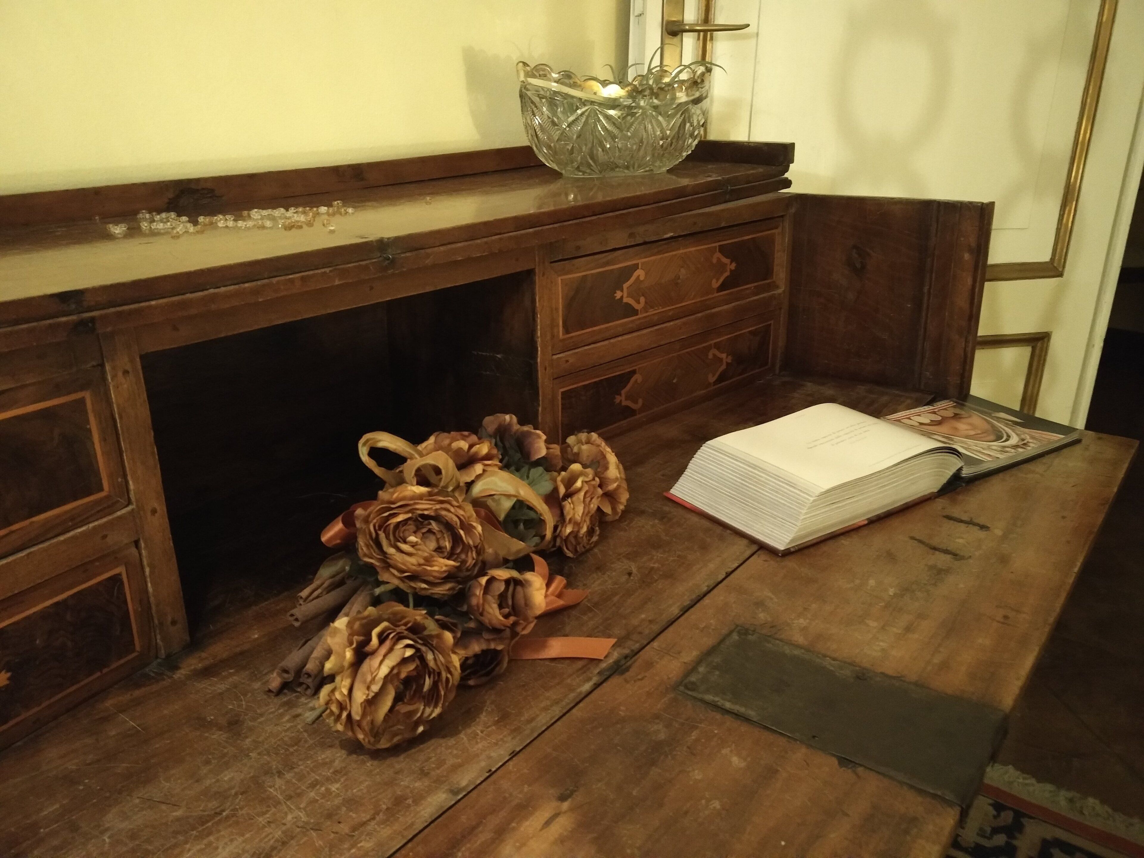 A wooden desk with a glass bowl, a book, and dried flowers.