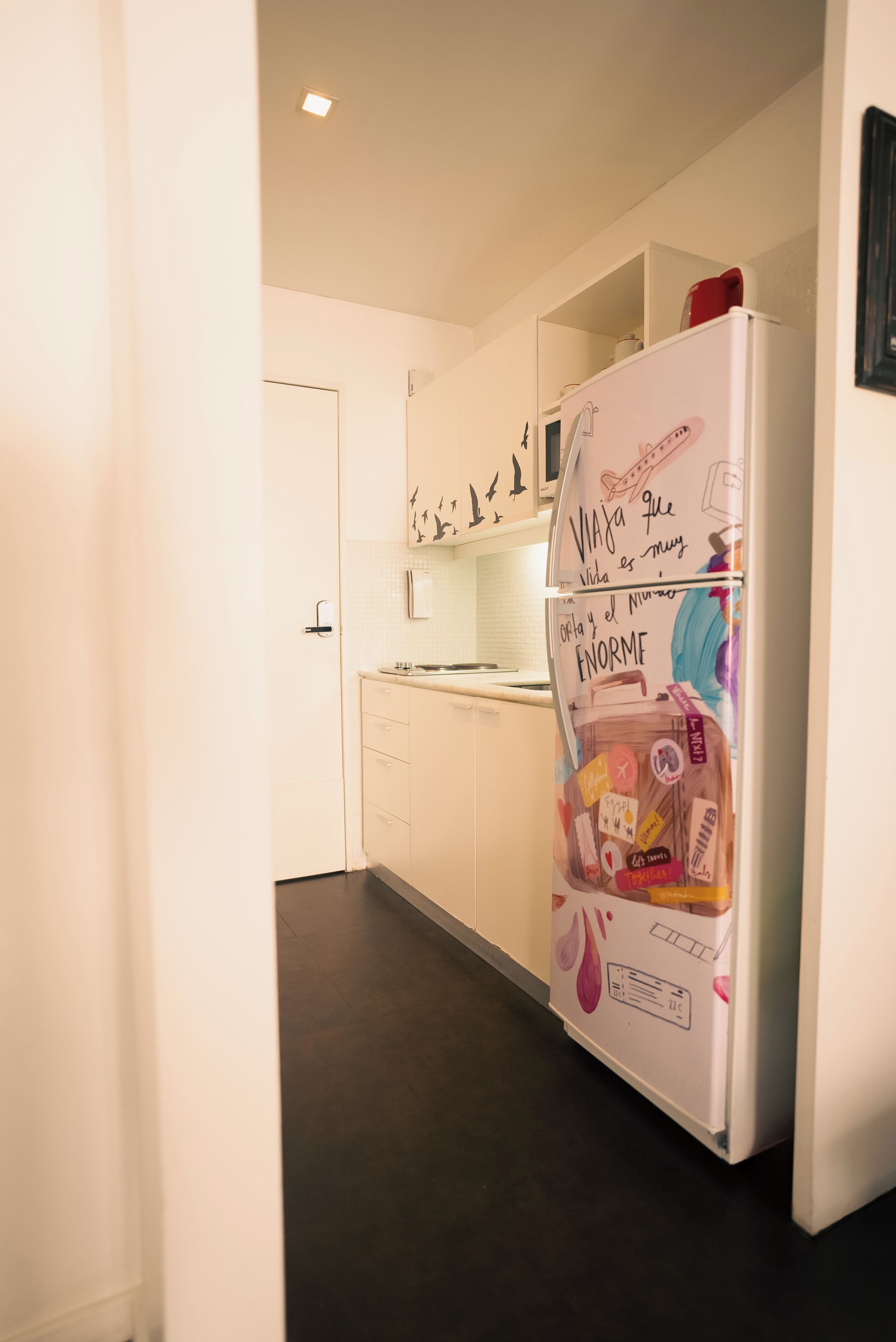 A kitchen with white cabinets, a white refrigerator with colorful magnets, and a tiled backsplash.