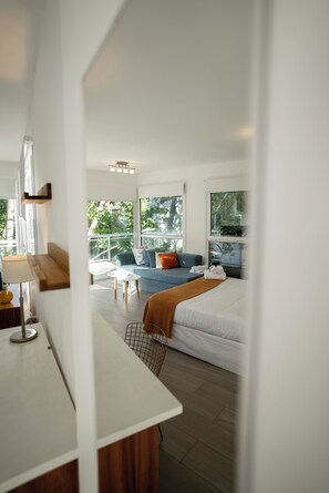 A modern hotel room with a bed, a sofa, a small table, and a balcony with a view of trees. - Sucre Suites (Buenos Aires)