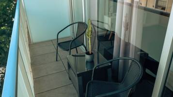 Un balcón con dos sillas, una mesa, una planta en maceta y un ventanal con cortinas.
