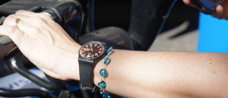 A close-up of a person's hand on a motorcycle handlebar, wearing a watch and a bracelet.