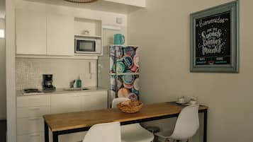A modern kitchen with white cabinets, a wooden dining table, and two white chairs. There is a hanging light fixture above the table and a chalkboard with writing on the wall.