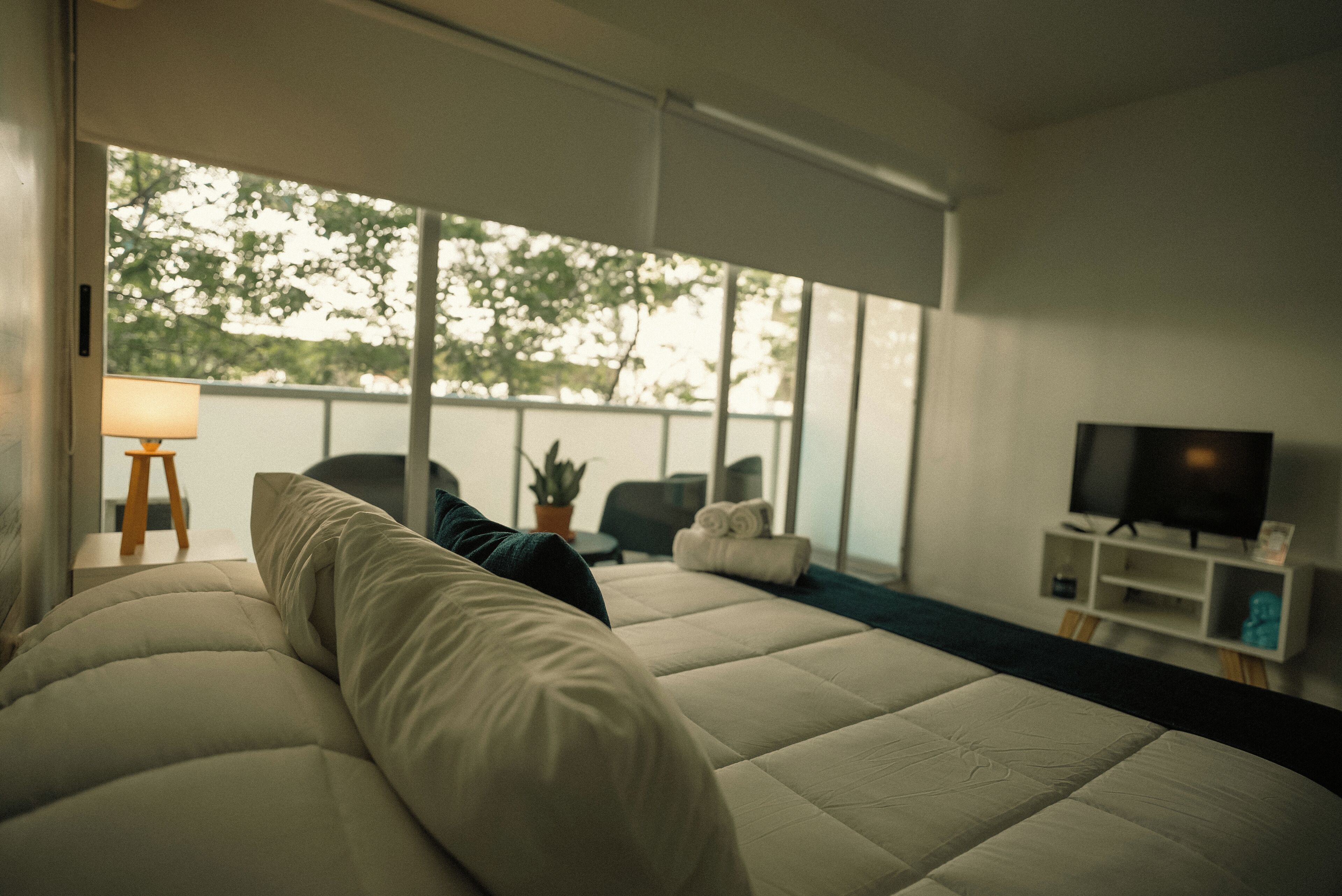 Un dormitorio moderno con una cama grande, un televisor y vistas a árboles a través de amplios ventanales.