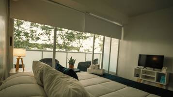 Un dormitorio moderno con una cama grande, un televisor y vistas a árboles a través de amplios ventanales.