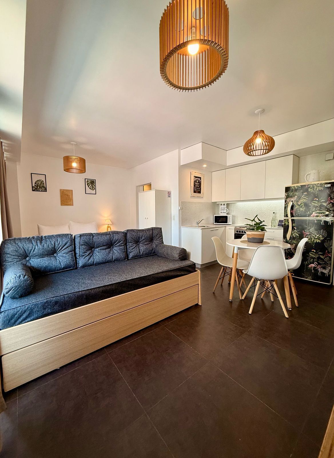 A modern living room with a sofa, dining table, chairs, and a kitchen area.