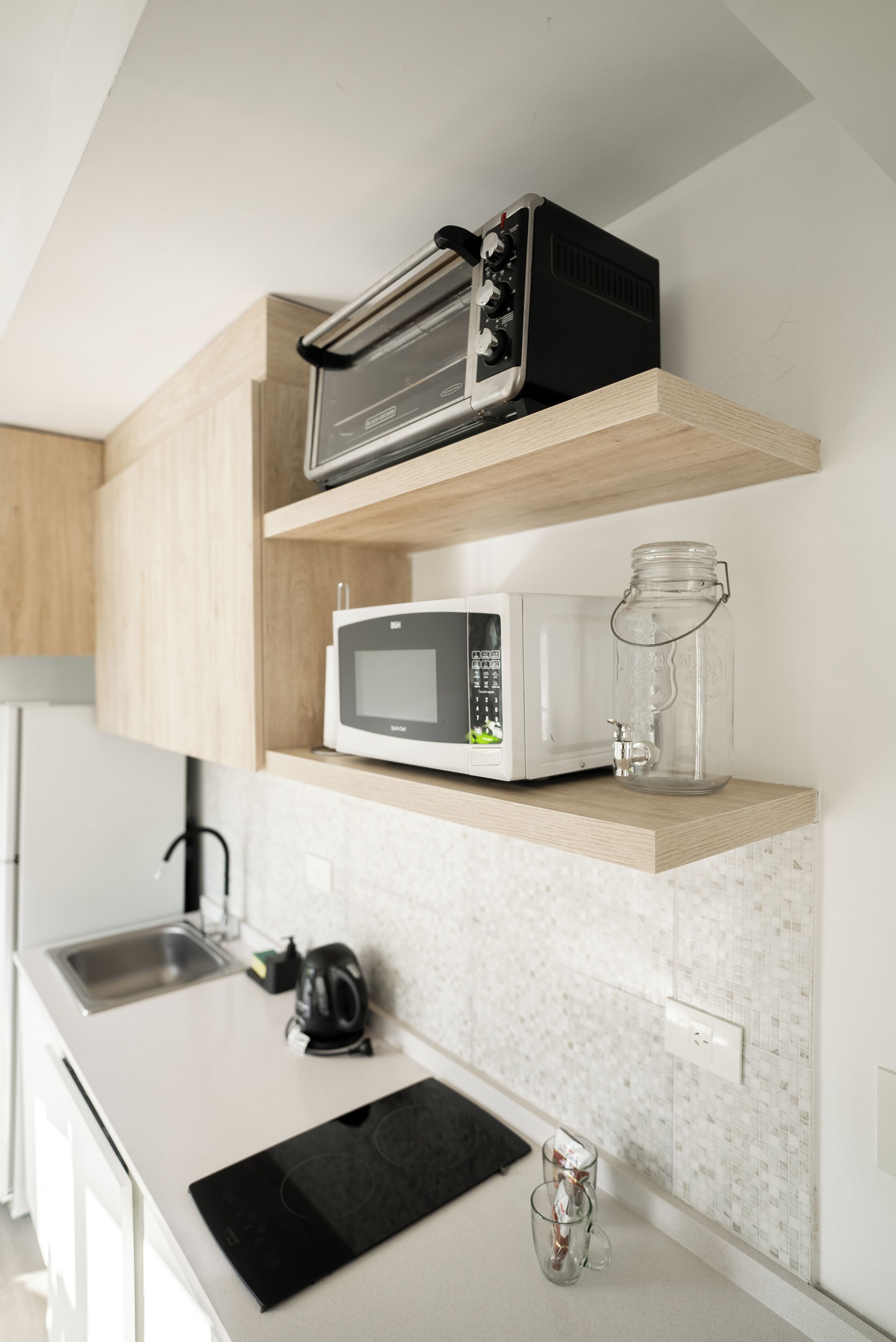 A kitchen with a microwave, toaster, and a glass jar on a shelf.
