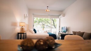 A hotel room with a bed, a desk with a computer, a TV, and a window with a view of trees. - Sucre Suites (Buenos Aires)