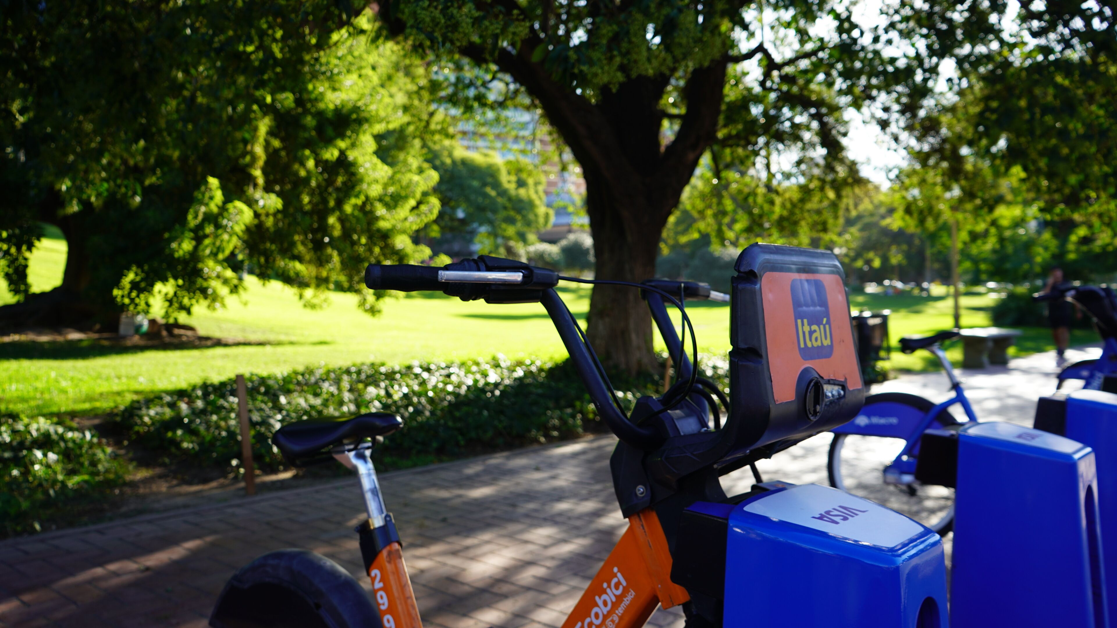 A stationary electric bike with a charging station and a blue box labeled "VISA" in a park.