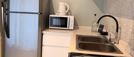 A compact kitchen with a stainless steel refrigerator, a microwave, a gas stove, and a sink.
