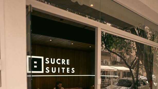 A hotel entrance with a reception desk, a visible interior with a plant, and a car parked outside. - Sucre Suites (Buenos Aires)
