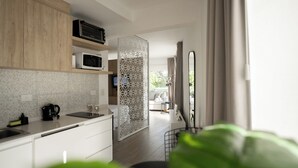 A modern kitchen with wooden cabinets, a microwave, and a kettle. There is a decorative white partition and a view of a balcony with a sofa. - Sucre Suites (Buenos Aires)