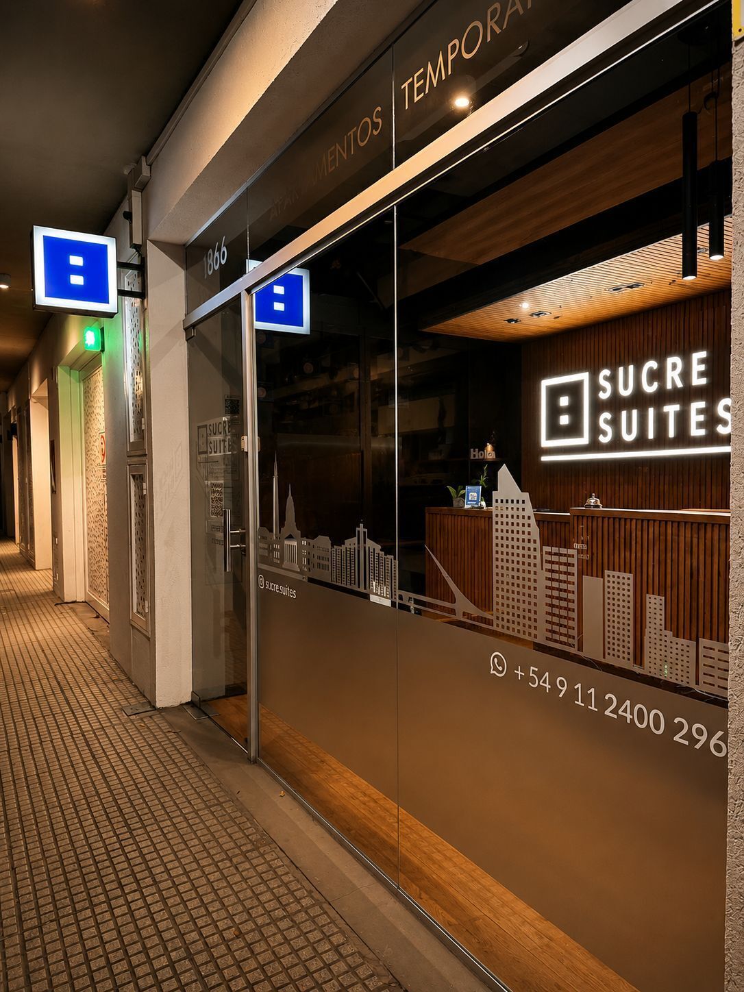 Entrada de hotel con fachada de vidrio, un mostrador de recepción y vistas a la ciudad.