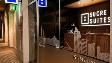 Entrada de hotel con fachada de vidrio, un mostrador de recepción y vistas a la ciudad.