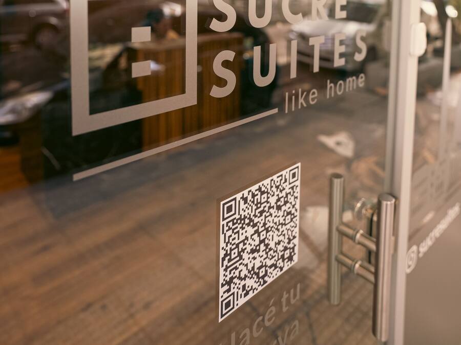 Een raam met de tekst 'SUCRE SUITES like home' en een QR-code.