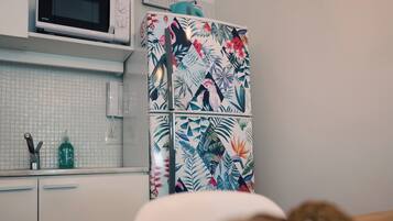 A kitchen with a microwave, a refrigerator with a tropical print, and a wooden table with a decorative item.