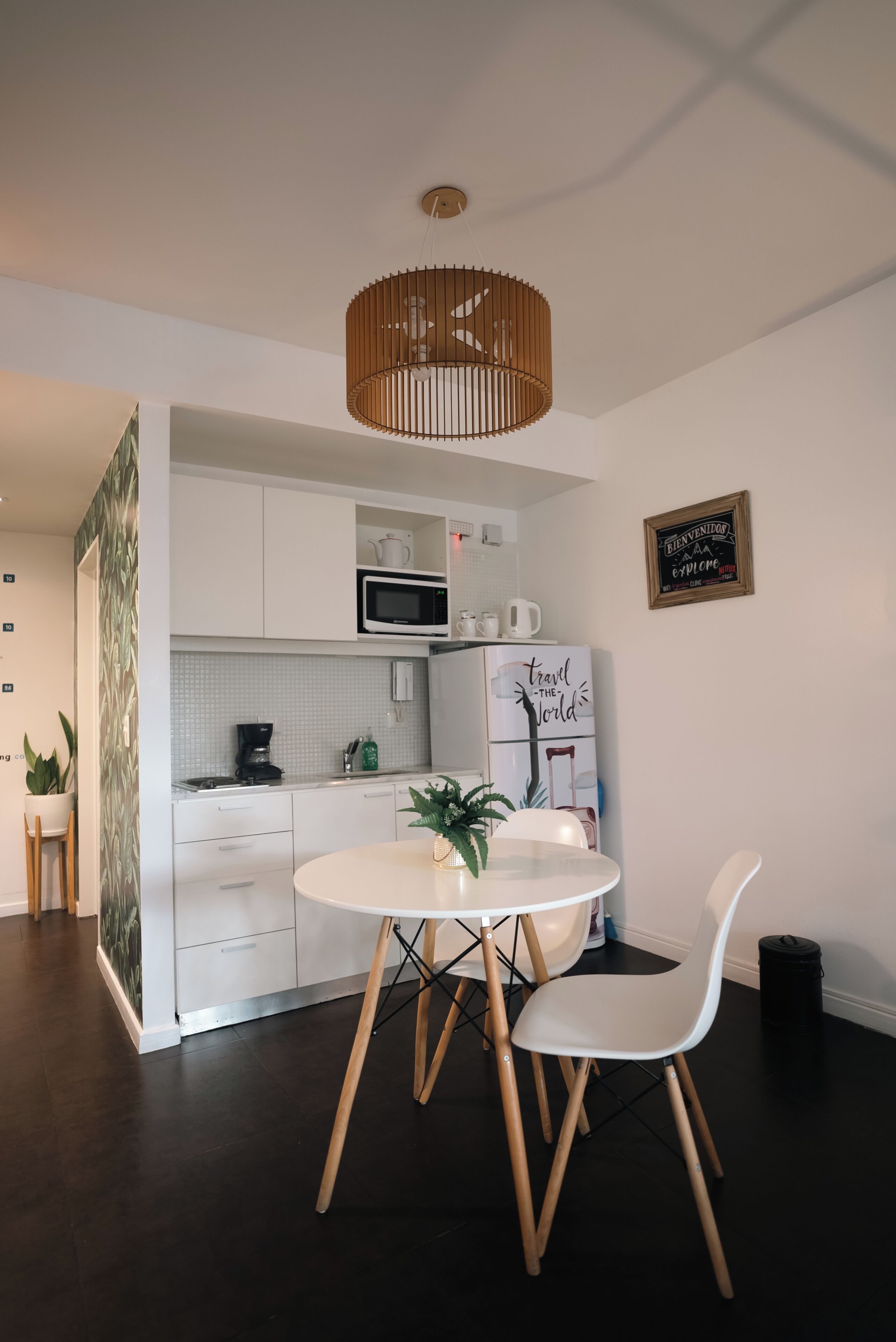 Een moderne keuken met witte kasten, een magnetron en een koffiezetapparaat. Er staat een eettafel met twee witte stoelen en een potplant.