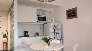Een moderne keuken met witte kasten, een magnetron en een koffiezetapparaat. Er staat een eettafel met twee witte stoelen en een potplant.