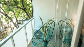 Un balcón con barandilla de vidrio, una planta en maceta y dos sillas de estructura metálica verde.