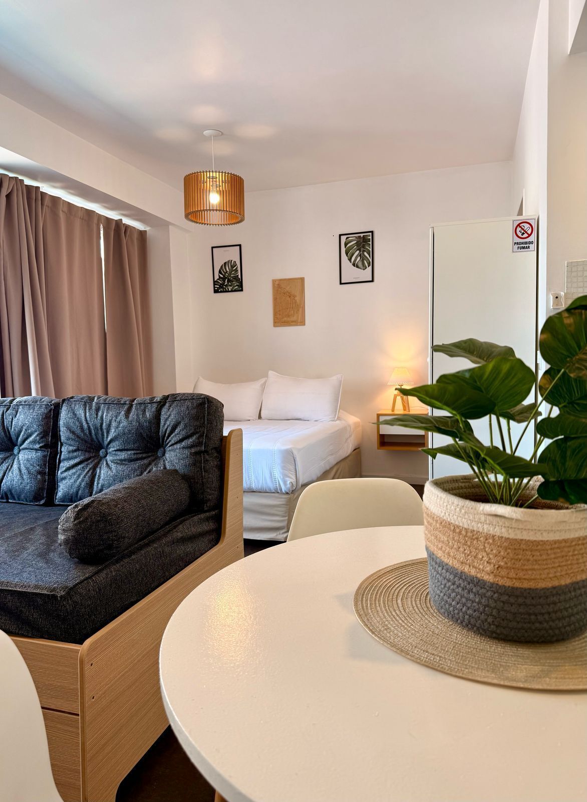 A modern hotel room with a sofa, a bed, a round table, and a potted plant.