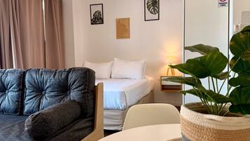 A modern hotel room with a sofa, a bed, a round table, and a potted plant.