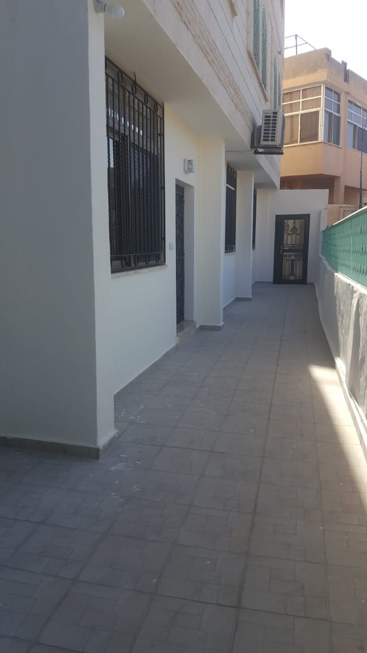 A corridor with tiled flooring, a gated entrance, and a building with a balcony.