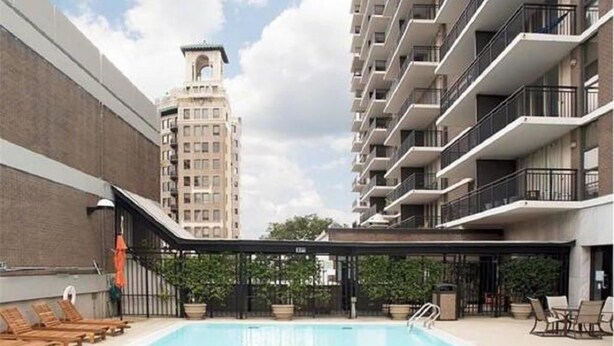 Piscina com espreguiçadeiras e área coberta, cercada por edifícios altos.
