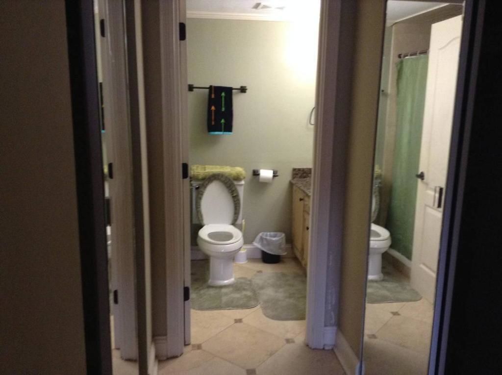 A narrow hallway leading to a bathroom with a toilet, a towel rack, and a shower area.