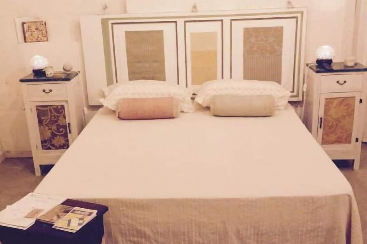 Ein Doppelbett mit weißer Bettdecke und zwei Kissen, an beiden Seiten Nachttische mit Lampen und ein kleiner Tisch mit einer Zeitschrift.