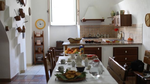 A kitchen with a dining table set for a meal, a clock on the wall, and various kitchen utensils and appliances. - Bnb Dragonetti (Manduria)