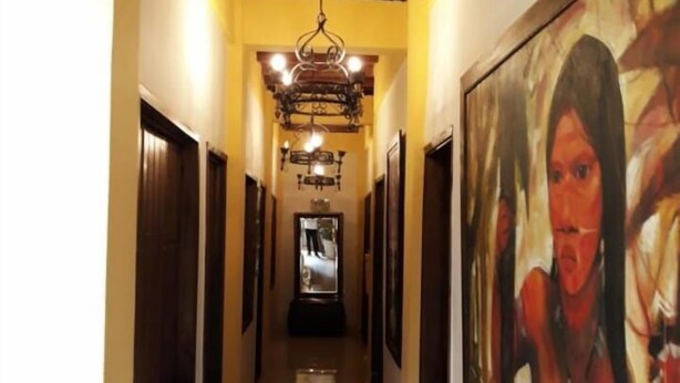 A hallway with a wooden ceiling, a chandelier, and a large painting on the right wall. - Hotel La Cosecha (Pereira)