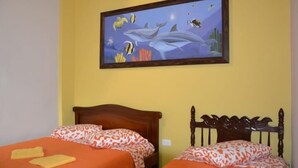 A room with two beds, each with an orange bedspread and matching pillows. Above the beds is a framed picture of marine life. - Hotel La Cosecha (Pereira)
