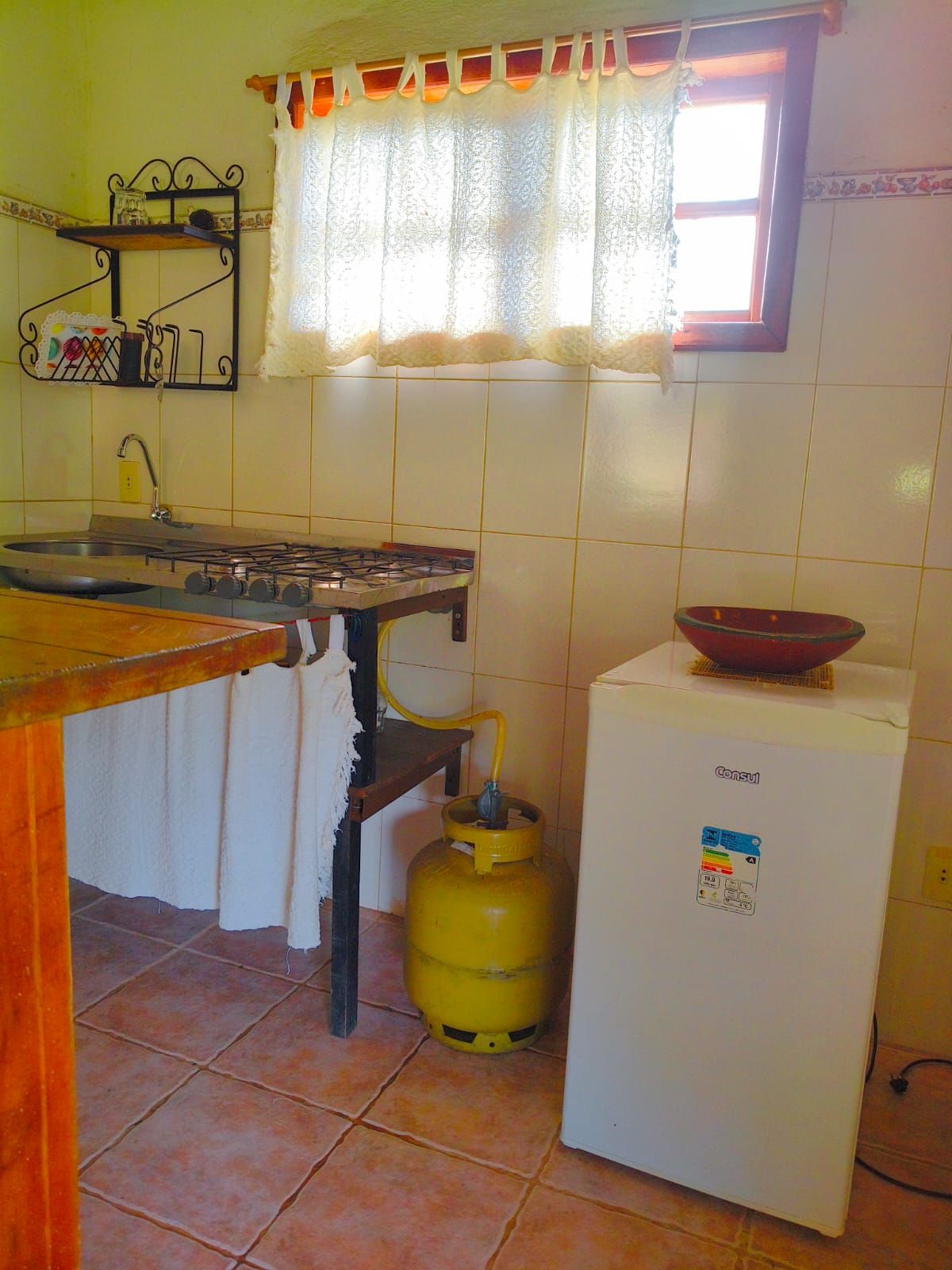 Cozinha com fogão a gás, geladeira, cilindro de gás e janela com cortina.