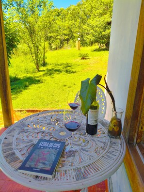 A round table with a book, a wine bottle, and glasses on a balcony overlooking a grassy area. - Pousada Chalés Barriga Da Lua (Santana do Riacho)