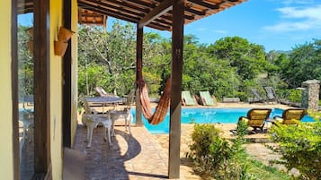 A covered outdoor area with a pool, stone flooring, and outdoor furniture.