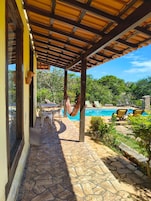 Espaço coberto ao ar livre com piscina, piso de pedra e mobiliário de exterior.