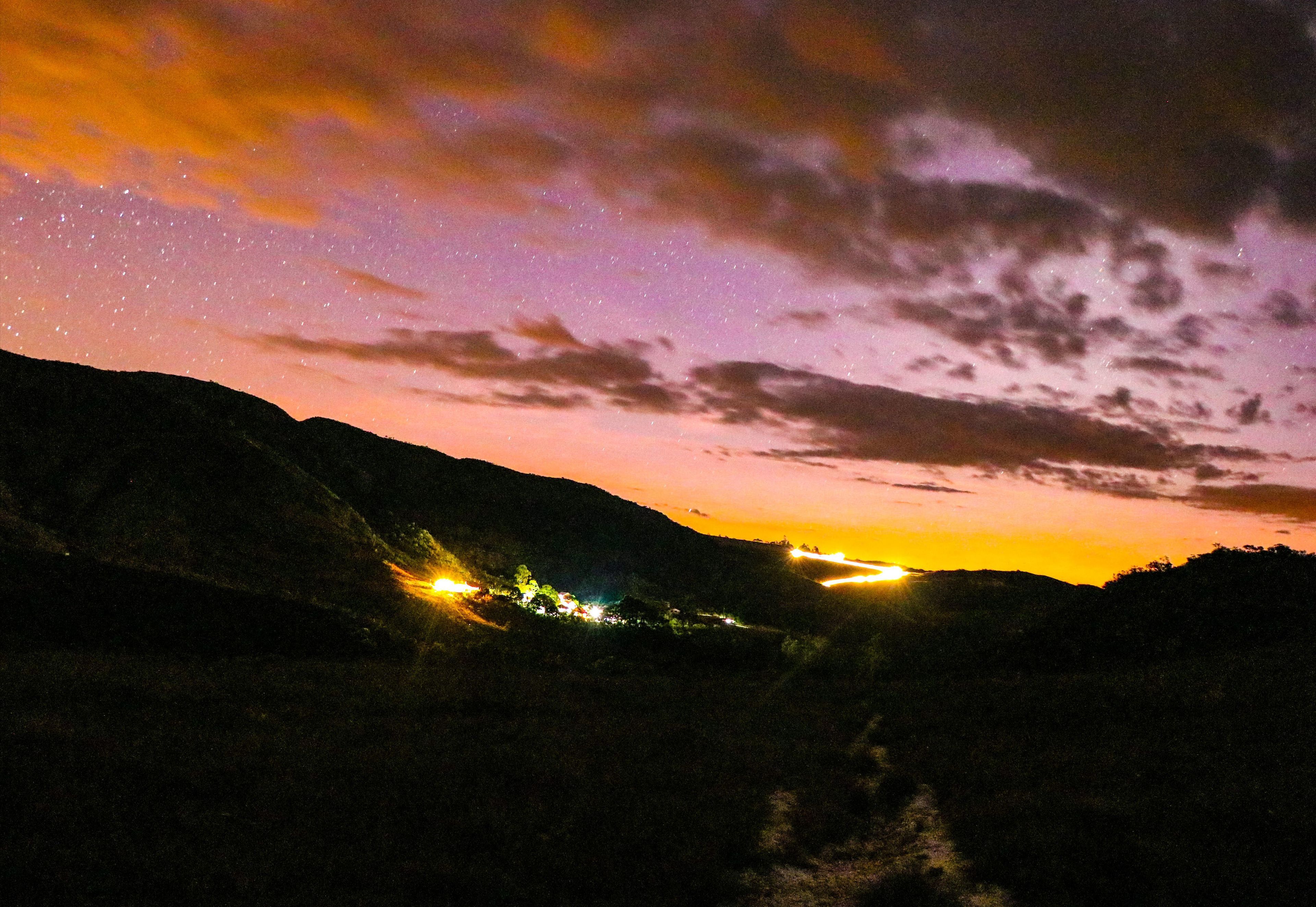 A night sky with stars and a sunset over a mountainous landscape.