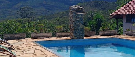 Una piscina con sillas de descanso, un pilar de piedra y montañas al fondo.