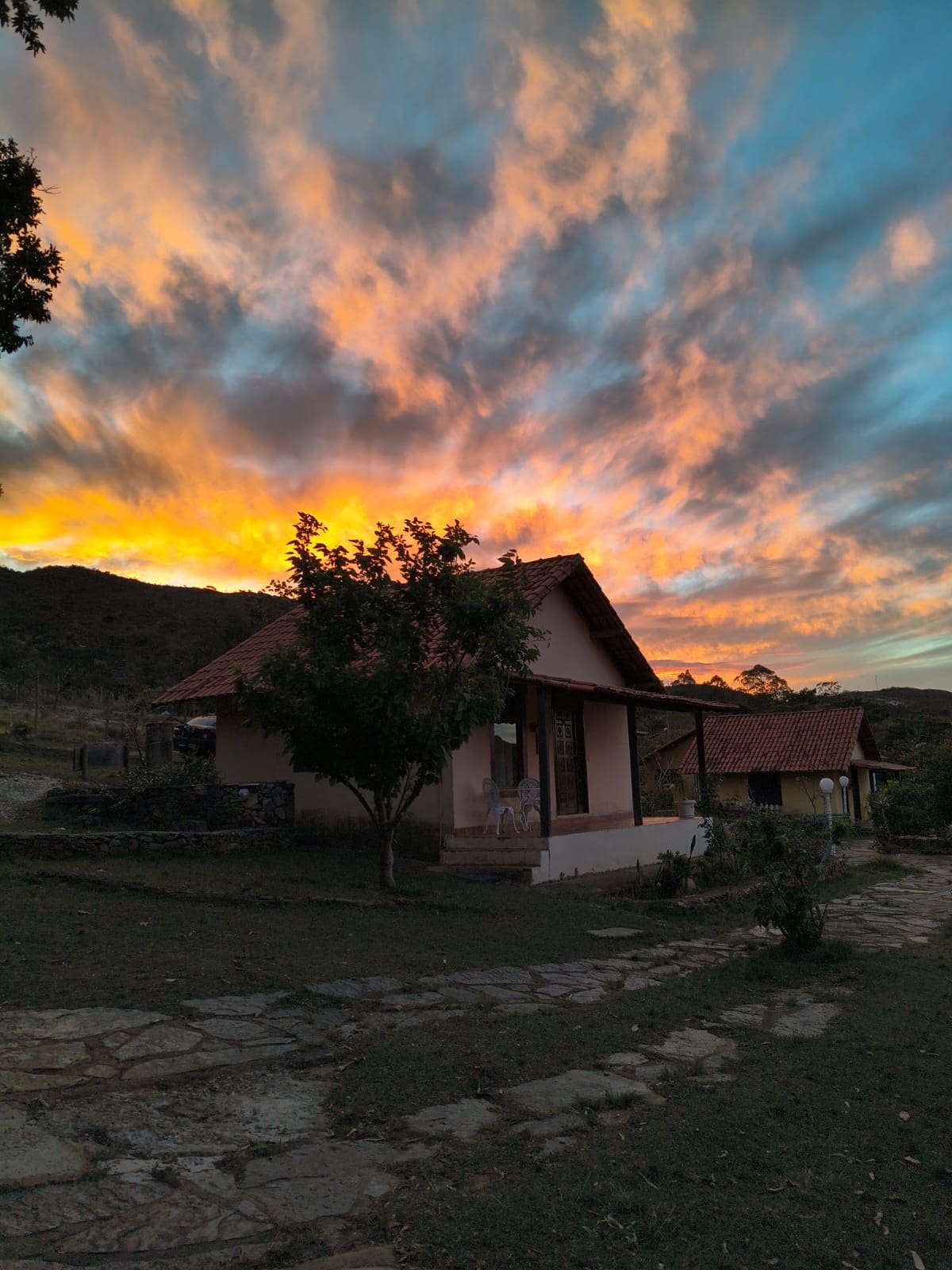Uma casa com telhado de cerâmica, varanda com cadeiras e um caminho de pedra que leva à entrada.