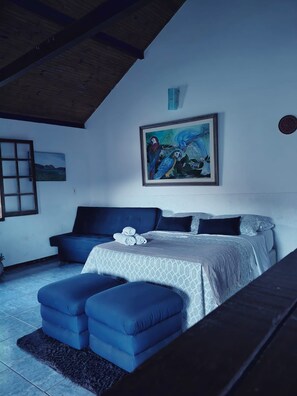 A bedroom with a bed, a sofa, a painting, and a window. - Pousada Chalés Barriga Da Lua (Santana do Riacho)