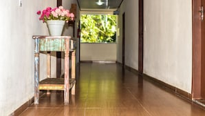 A hallway with a wooden floor, a chair with a flower pot, and a window with a view of greenery. - Pousada Colibri (Paraty)