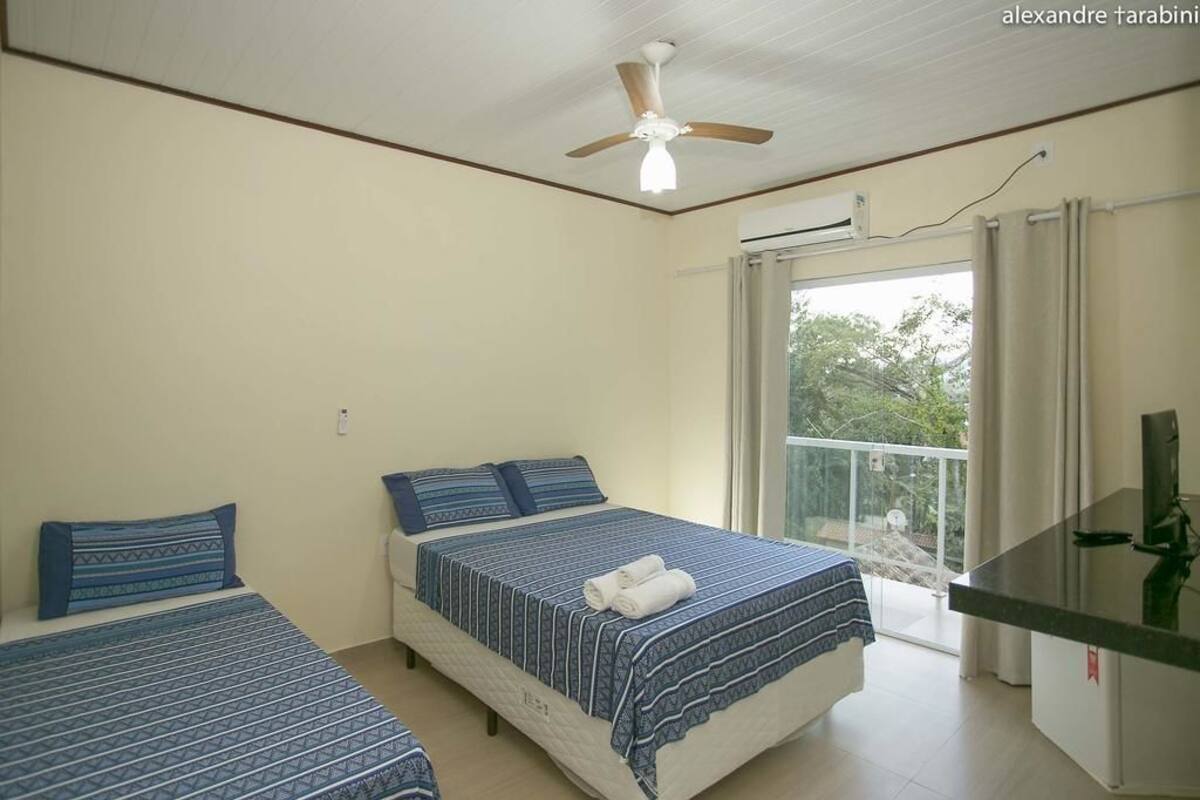 A bedroom with two beds, a ceiling fan, a balcony with a glass door, and a small desk with a TV.