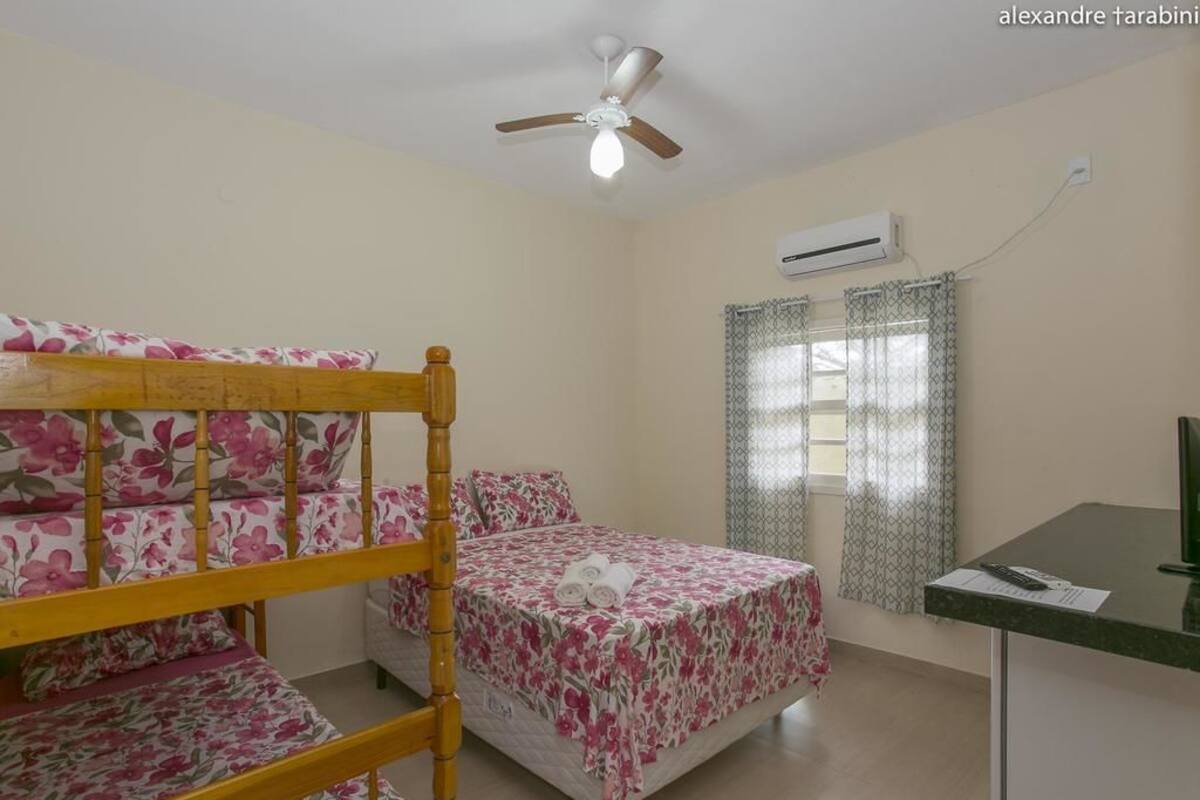 A room with bunk beds, a desk, an air conditioning unit, and a window with patterned curtains.