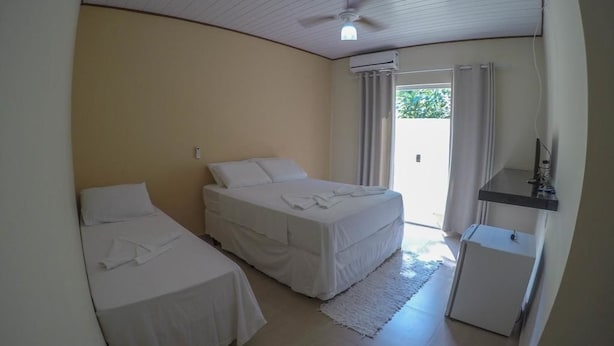 A room with two beds, a ceiling fan, an air conditioning unit, a small desk, and a view of the outside. - Pousada Colibri (Paraty)