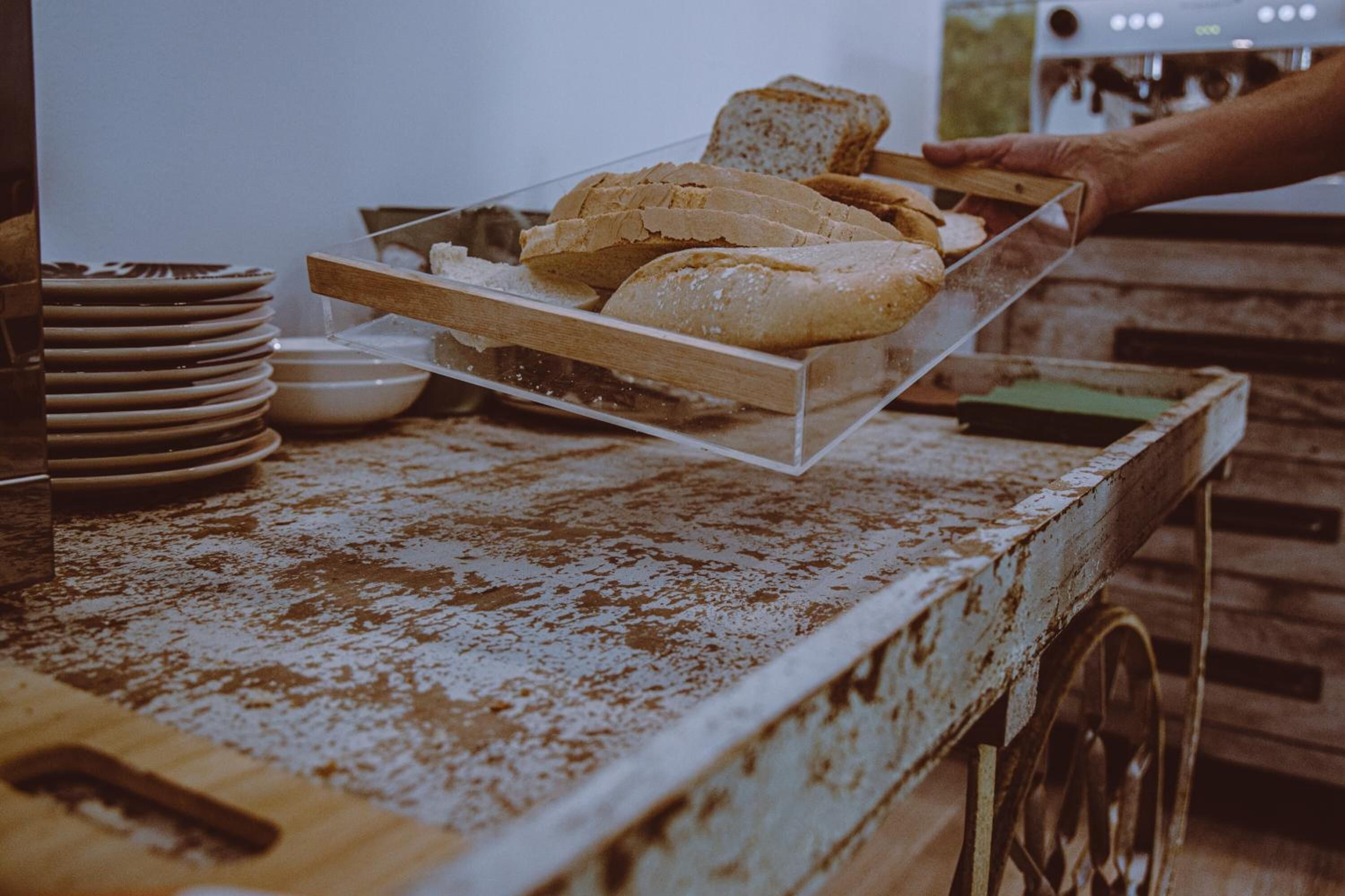 A hand placing a clear plastic tray with bread on a rustic wooden table.